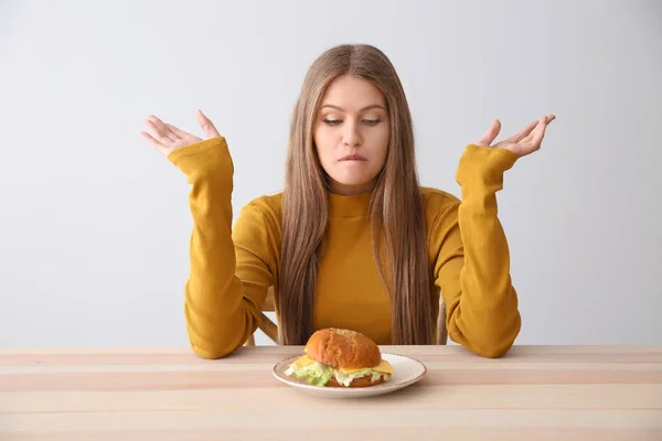 Jeune femme émotionnelle avec hamburger savoureux à table — Photo