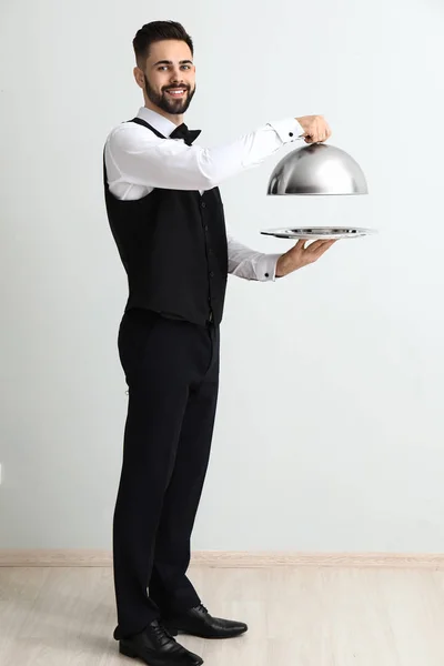 Waiter with tray and cloche near light wall — Stock Photo, Image