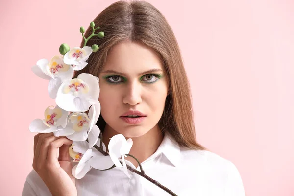 Hermosa mujer joven con maquillaje brillante y flores en el fondo de color — Foto de Stock