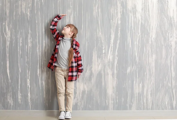 Μέτρηση ύψους κοντά γκρίζο τοίχο το χαριτωμένο μικρό κορίτσι — Φωτογραφία Αρχείου