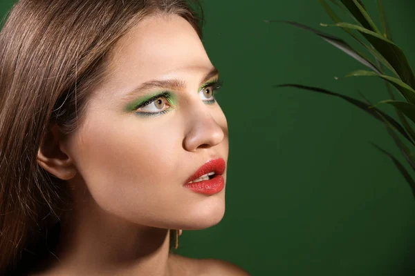 Hermosa mujer joven con maquillaje brillante y hoja tropical sobre fondo de color — Foto de Stock