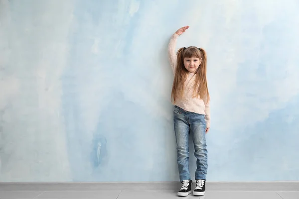 Linda niña midiendo altura cerca de la pared de color — Foto de Stock