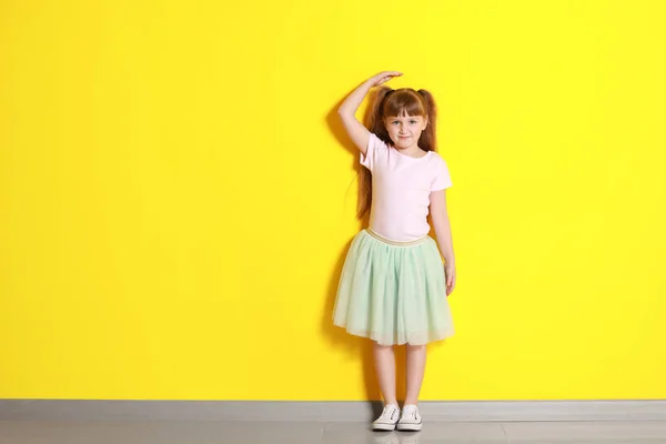 Cute little girl measuring height near color wall — Stock Photo, Image