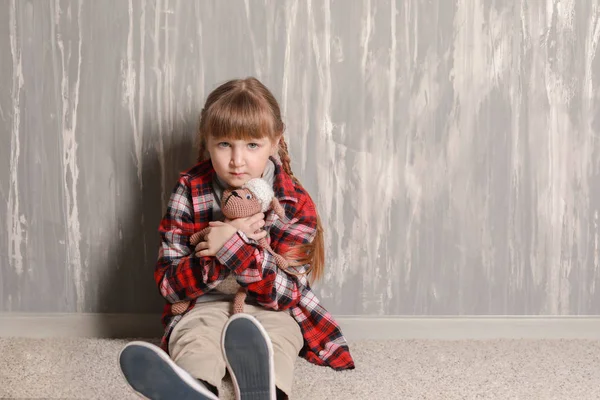 Sad little girl sitting on floor near grey wall — Stock Photo, Image