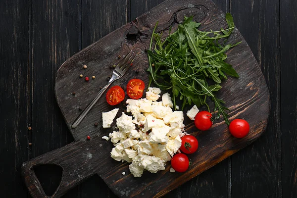 Tasty feta cheese with tomatoes and arugula on wooden board — Stock Photo, Image