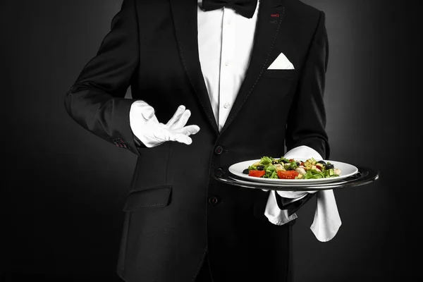Bel cameriere con insalata fresca su sfondo scuro — Foto Stock