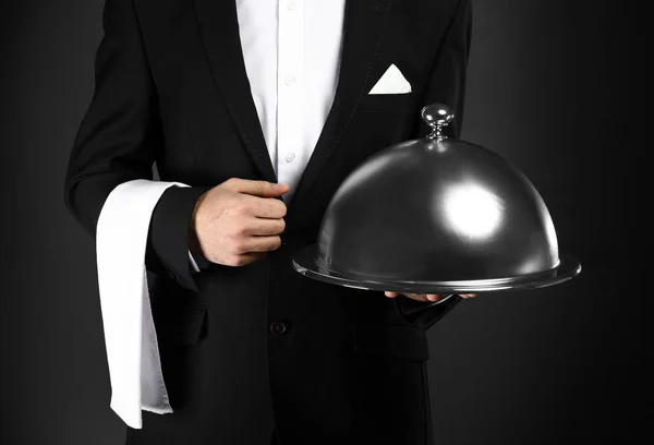 Handsome waiter with tray and cloche on dark background — Stock Photo, Image