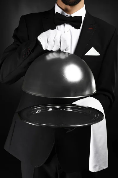 Bellissimo cameriere con vassoio e cloche su sfondo scuro — Foto Stock