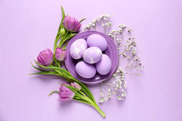 Piatto con uova di Pasqua e tulipani su sfondo colore — Foto Stock