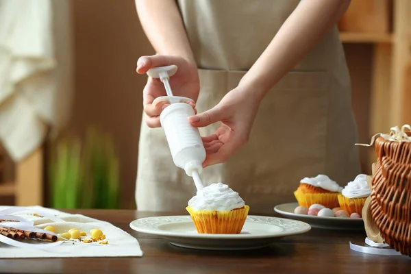 Woman preparing tasty Easter cupcake in kitchen