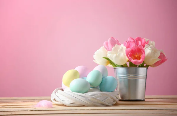 Nido con uova di Pasqua e fiori sul tavolo sullo sfondo di colore — Foto Stock