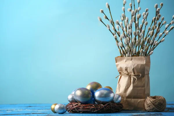 Nest with Easter eggs and pussy willow branches on table against color background — Stock Photo, Image