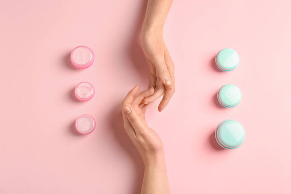 Female hands with jars of natural cream on color background