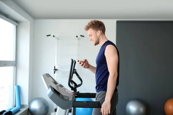 Sporty young man listening to music while training on treadmill in gym — Stock Photo, Image