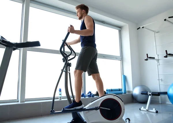 Sporty young man training on machine in gym — Stock Photo, Image