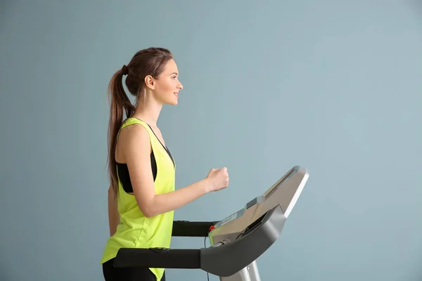 Sporty young woman training on treadmill against color background — Stock Photo, Image