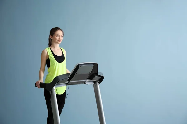 Sporty young woman training on treadmill against color background — Stock Photo, Image