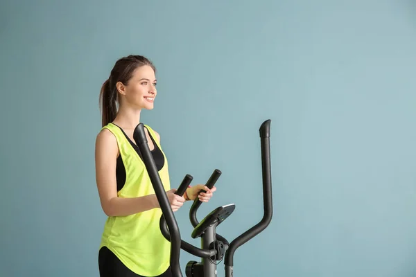 Sporty young woman training on machine against color background — Stock Photo, Image