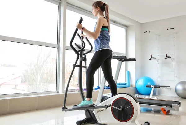 Sporty young woman training on machine in gym — Stock Photo, Image