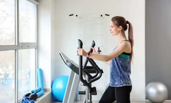 Sporty young woman training on machine in gym — Stock Photo, Image