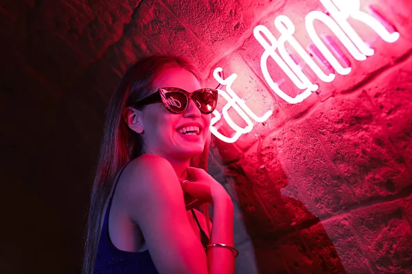Portrait of beautiful young woman standing near neon lighting on wall — Stock Photo, Image