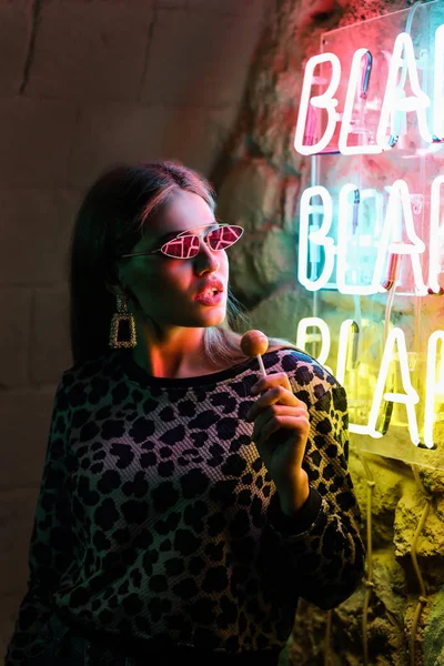 Portrait of beautiful young woman standing near neon lighting on wall — Stock Photo, Image