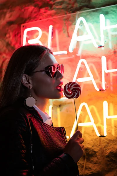 Portrait of beautiful young woman standing near neon lighting on wall — Stock Photo, Image