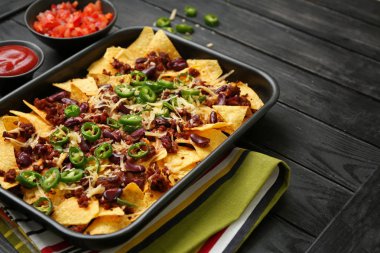 Ahşap masada lezzetli nachos, kıyılmış et ve Chili ile pişirme çanak