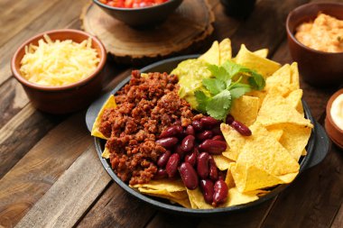 Ahşap masada lezzetli nachos, kıyılmış et, fasulye ve guacamole ile tava