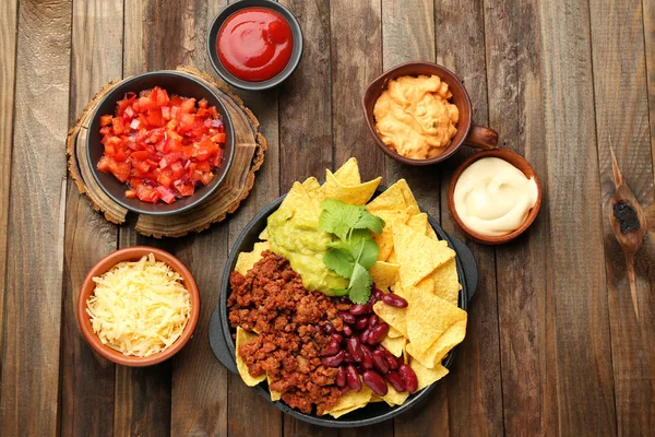 Frying pan with tasty nachos, minced meat, beans and guacamole on wooden table — Stock Photo, Image