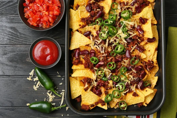 Prato de panificação com nachos saborosos, carne picada e pimenta na mesa de madeira — Fotografia de Stock