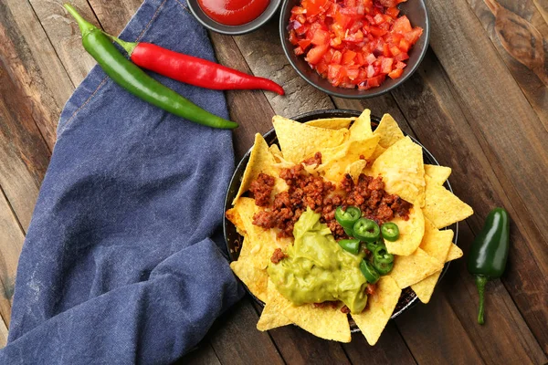 Frying pan with tasty nachos, minced meat, chili and guacamole on wooden table — Stock Photo, Image