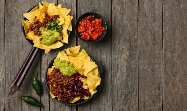 Frying pans with tasty nachos, minced meat, beans and guacamole on wooden table — Stock Photo, Image