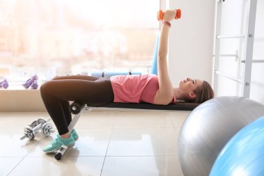 Spor salonunda dambıllarla spor yapan genç bir bayan.