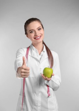 Işık arka planda başparmak-up gösteren Apple ile kadın beslenme uzmanı portresi