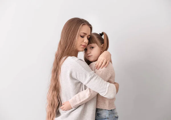 Sad woman after divorce hugging her little daughter against light background — Stock Photo, Image