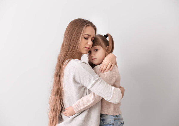 Sad woman after divorce hugging her little daughter against light background