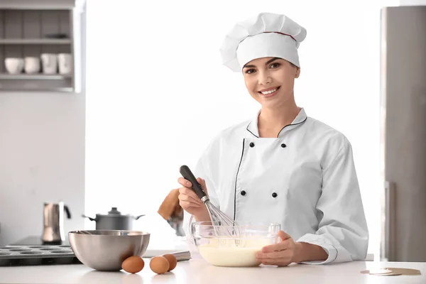 Young female confectioner making dough in kitchen