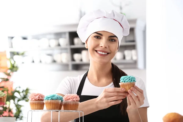 Confeiteiro feminino jovem com cupcakes saborosos na cozinha — Fotografia de Stock