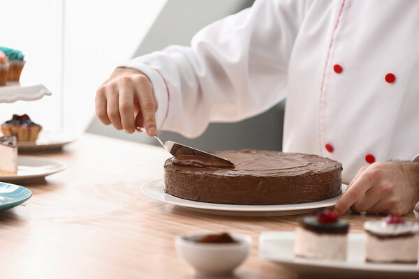 Male confectioner decorating tasty chocolate cake in kitchen, closeup