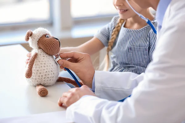 Pediatrician with toy showing little girl how to use stethoscope in clinic — Stock Photo, Image