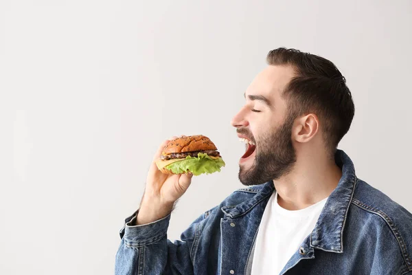 Man eating tasty burger on light background