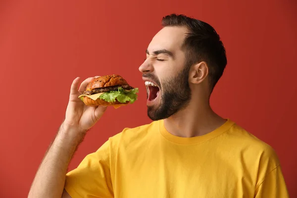 Hombre comiendo sabrosa hamburguesa sobre fondo de color — Foto de Stock