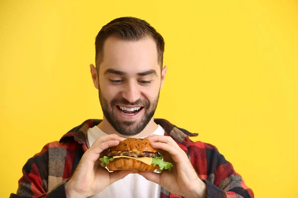 Mann mit leckerem Burger auf farbigem Hintergrund — Stockfoto