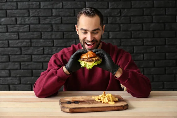 Mann isst leckeren Burger mit Pommes am Tisch — Stockfoto