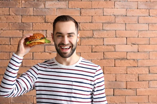 Homme avec hamburger savoureux contre le mur de briques — Photo