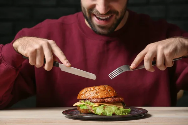 Mann isst leckeren Burger am Tisch — Stockfoto