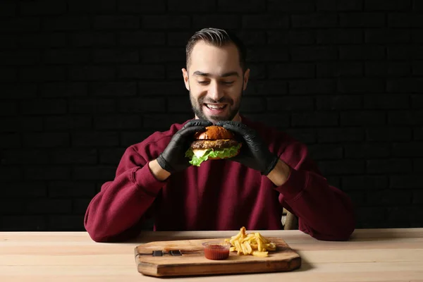 テーブルでおいしいハンバーガーとフライド ポテトを食べる男 — ストック写真