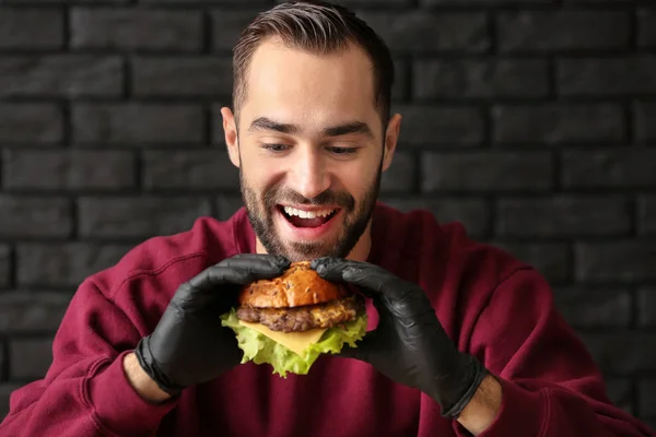 Hombre comiendo sabrosa hamburguesa sobre fondo oscuro —  Fotos de Stock