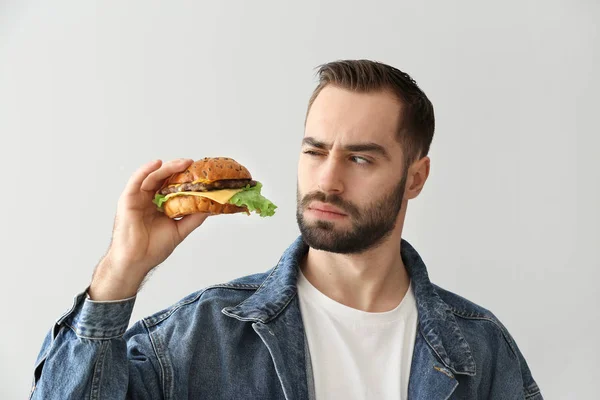 Uomo sospetto con gustoso hamburger su sfondo chiaro — Foto Stock